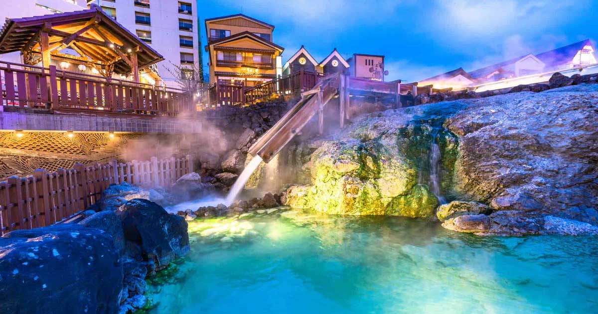 The Yubatake hot water field steaming mineral water cascading through wooden channels lit by warm light.